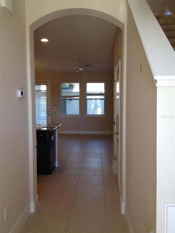 A tiled hallway leads through an arched doorway into a kitchen with dark cabinetry — 12349 VIA DERNA PLACE, WINDERMERE, FL
