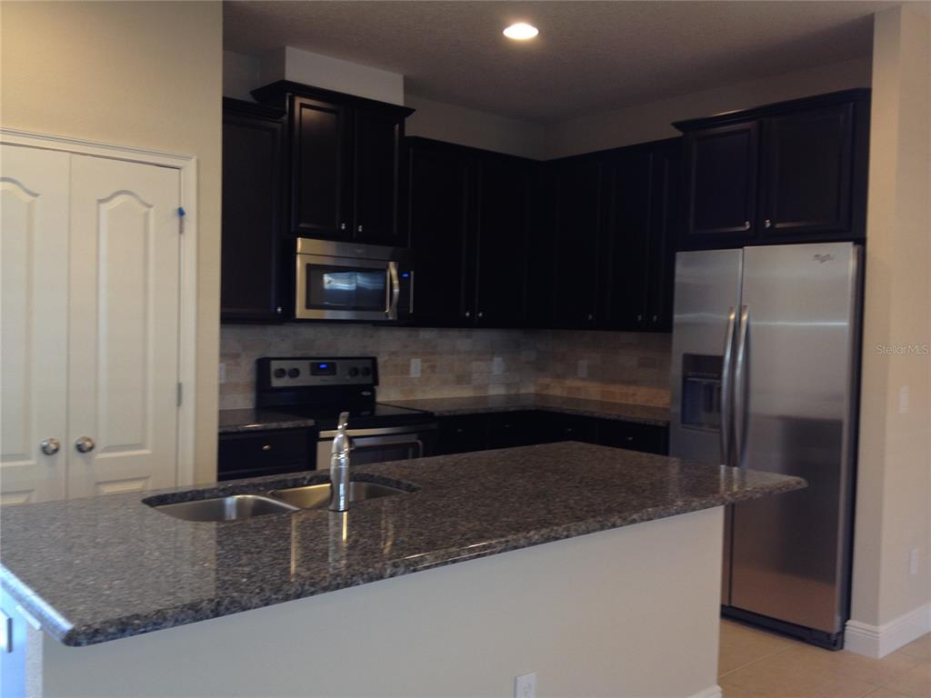 A kitchen features dark wood cabinets, granite countertops, stainless steel appliances, and a breakfast bar — 12349 VIA DERNA PLACE, WINDERMERE, FL