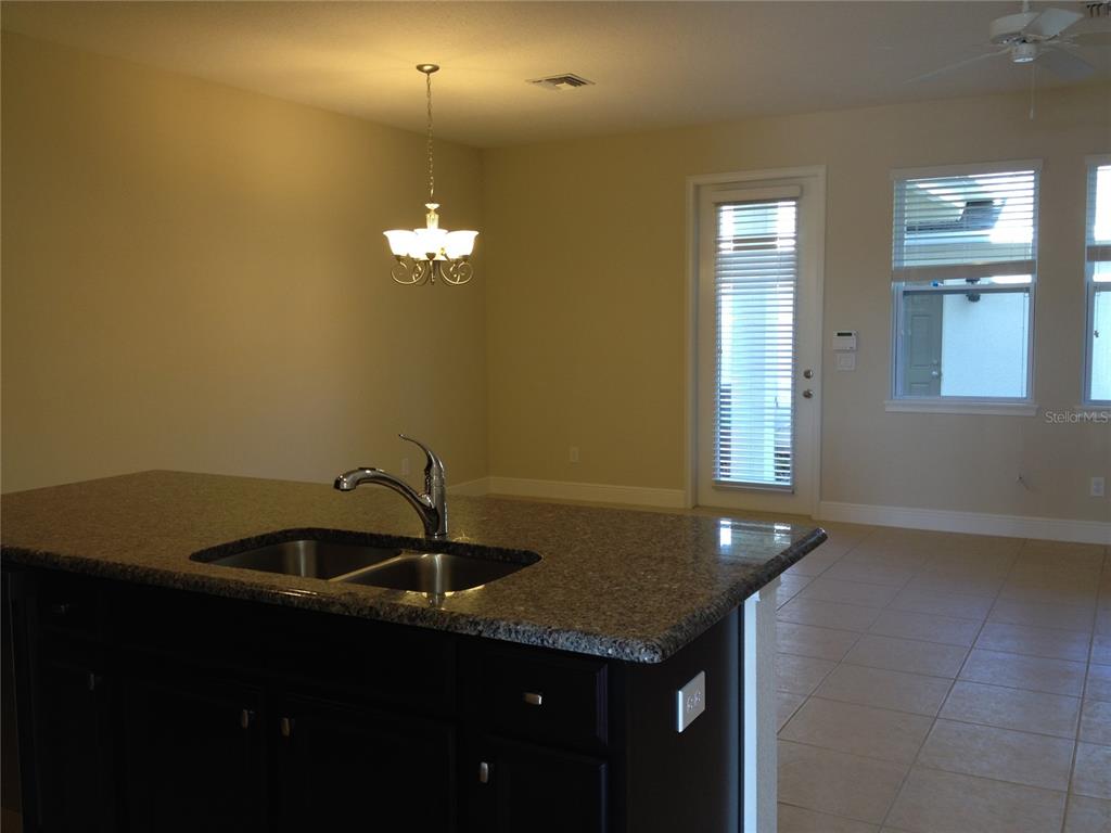 A kitchen island with a granite countertop and sink overlooks a dining area with tile — 12349 VIA DERNA PLACE, WINDERMERE, FL