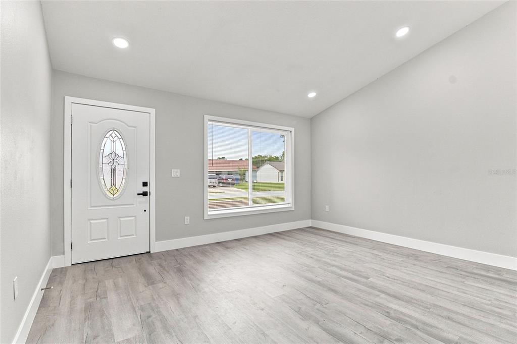A bright room features light gray walls, wood-look flooring, a front door, and a window — 7342 IVORY TERRACE, NEW PORT RICHEY, FL