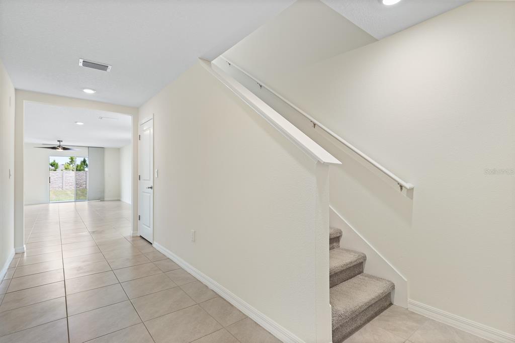 A hallway with tile flooring leads to an open living area past a carpeted staircase — 16555 MOSAIC OAR DRIVE, WIMAUMA, FL