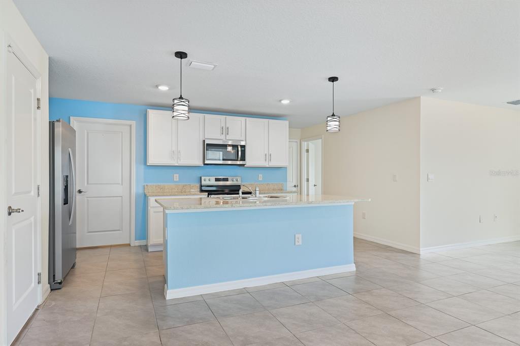 A kitchen features white cabinets, a light blue island, stainless steel appliances, and tile flooring — 16555 MOSAIC OAR DRIVE, WIMAUMA, FL