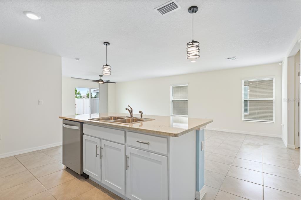 A kitchen island with a stainless steel dishwasher and sink sits in an open-concept room — 16555 MOSAIC OAR DRIVE, WIMAUMA, FL