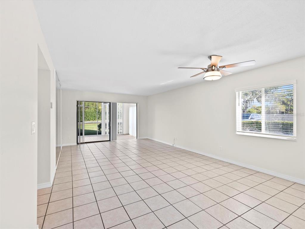 A bright, empty living room features white walls, light-colored tile flooring, and a ceiling fan — 2737 ENTERPRISE ROAD E UNIT 111, CLEARWATER, FL