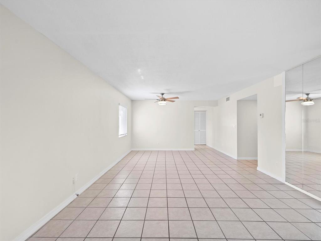 An empty room with light-colored tile flooring, white walls, a ceiling fan, and mirrored closet doors — 2737 ENTERPRISE ROAD E UNIT 111, CLEARWATER, FL