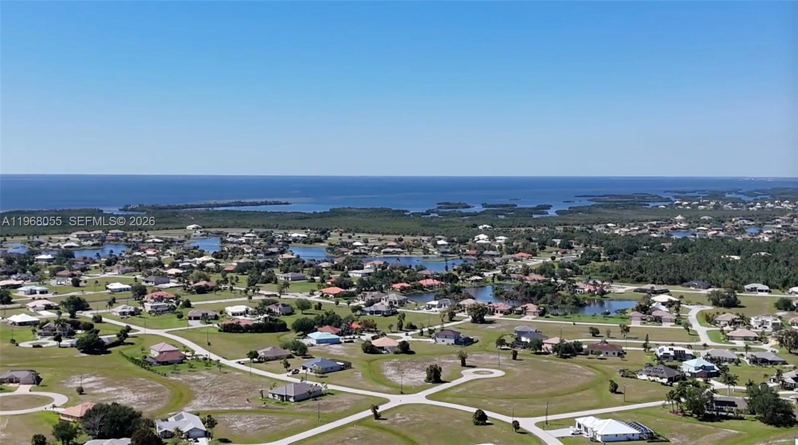 An aerial view shows a residential neighborhood with scattered houses near a large body of water — 17285 Acapulco rd, Punta Gorda FL 33955, PUNTA GORDA, FL