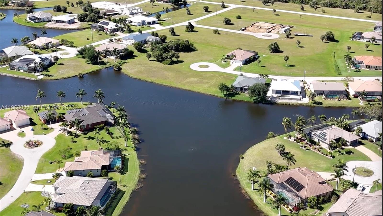 An aerial view shows several suburban houses situated around a large, central man-made lake — 17285 Acapulco rd, Punta Gorda FL 33955, PUNTA GORDA, FL