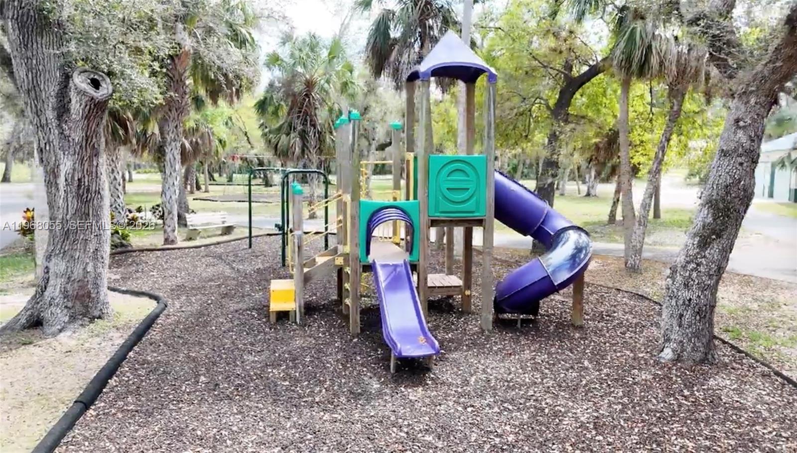 A colorful playground structure with two slides sits in a wooded area with mulch — 17285 Acapulco rd, Punta Gorda FL 33955, PUNTA GORDA, FL