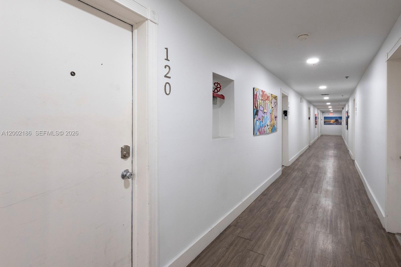 A long apartment hallway features white walls, wood-look flooring, and numbered unit doors — 335 Ocean Dr # 120, Miami Beach FL 33139, MIAMI BEACH, FL