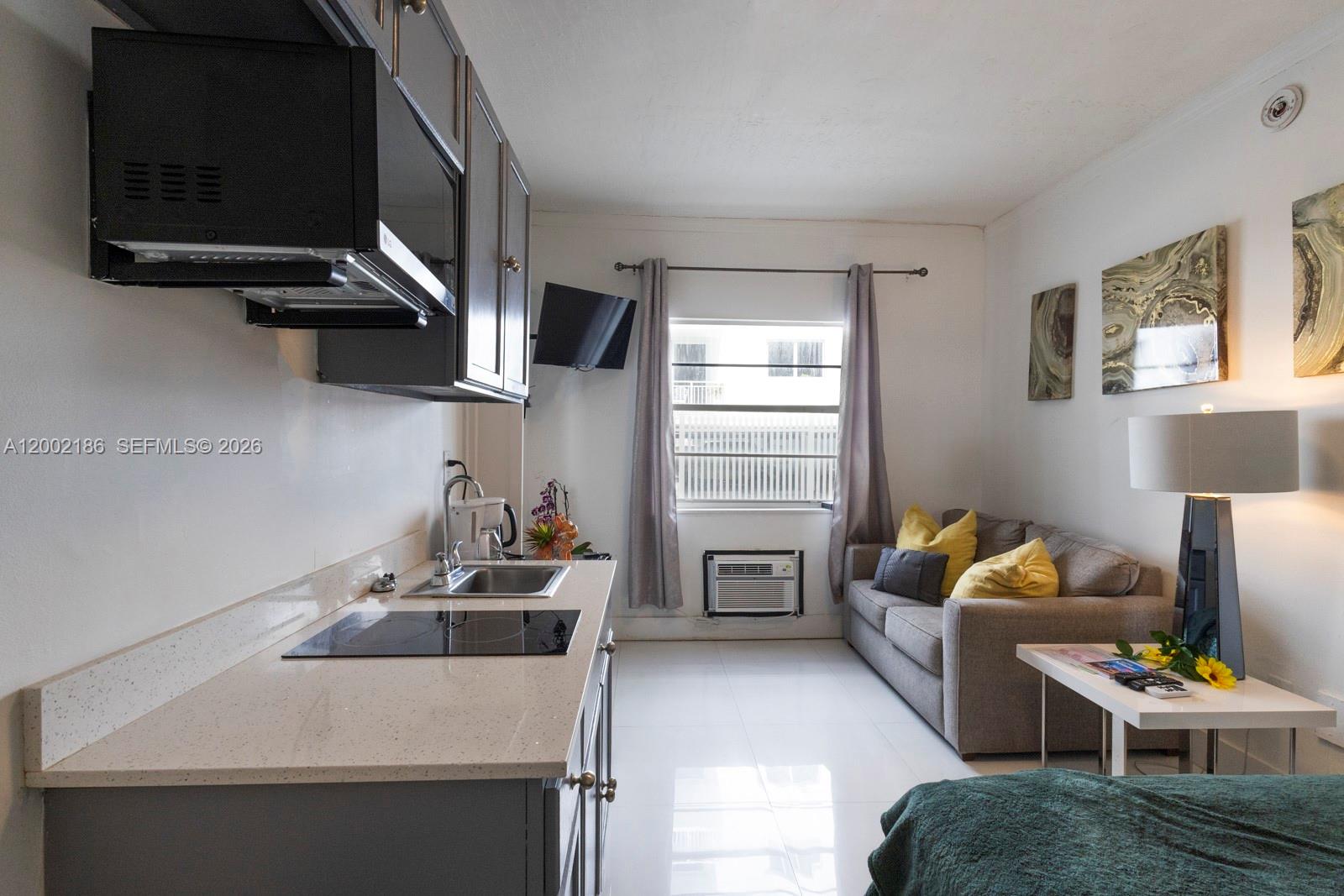 A studio apartment features a kitchenette with dark cabinets, a sofa, and a window — 335 Ocean Dr # 120, Miami Beach FL 33139, MIAMI BEACH, FL
