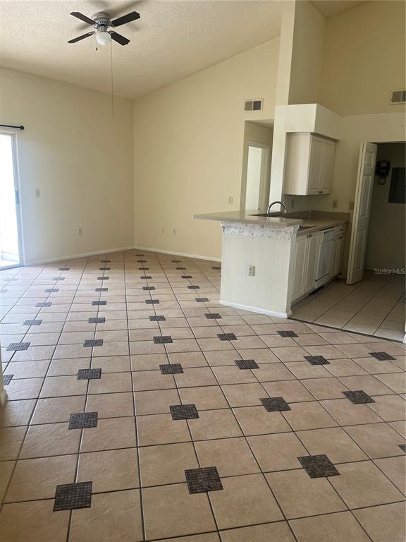 An open-concept living area features tan tile flooring with dark accents and a kitchen peninsula — 1205 BERMUDA LAKES LANE UNIT 303, KISSIMMEE, FL