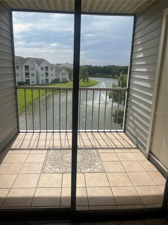 A screened-in balcony with tiled flooring overlooks a lake with a fountain and apartment buildings — 1205 BERMUDA LAKES LANE UNIT 303, KISSIMMEE, FL