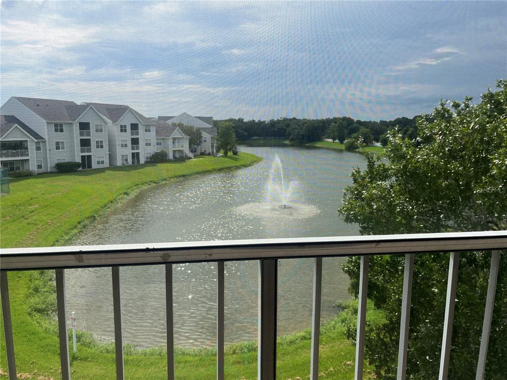 A view from a balcony overlooking a lake with a fountain and apartment buildings — 1205 BERMUDA LAKES LANE UNIT 303, KISSIMMEE, FL