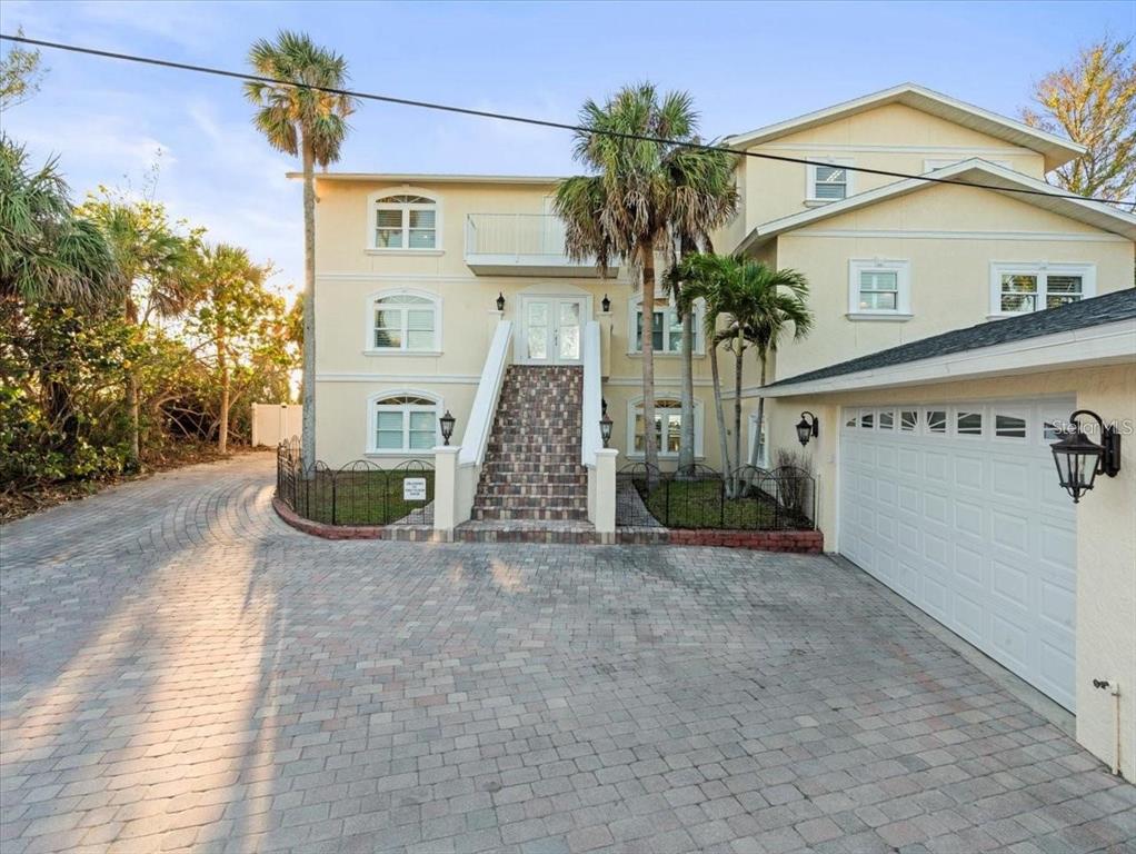 A three-story yellow house features a brick staircase leading to the front entrance and driveway — 8030 MANASOTA KEY ROAD, ENGLEWOOD, FL
