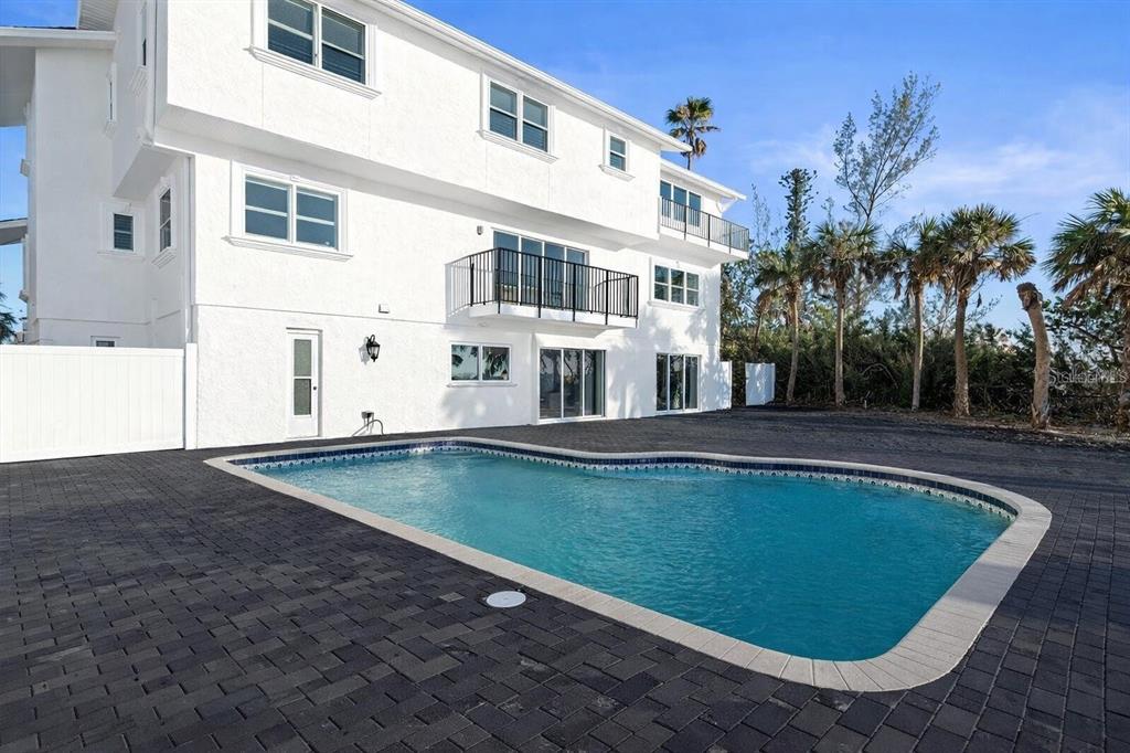 A white three-story house features a swimming pool set in a dark paver patio — 8030 MANASOTA KEY ROAD, ENGLEWOOD, FL