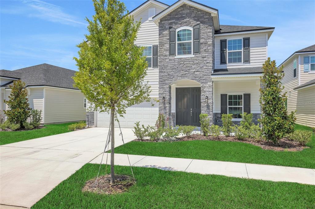 A two-story suburban house with a stone facade, dark double doors, and a concrete driveway — 3902 HOLSTEIN WAY, GREEN COVE SPRINGS, FL