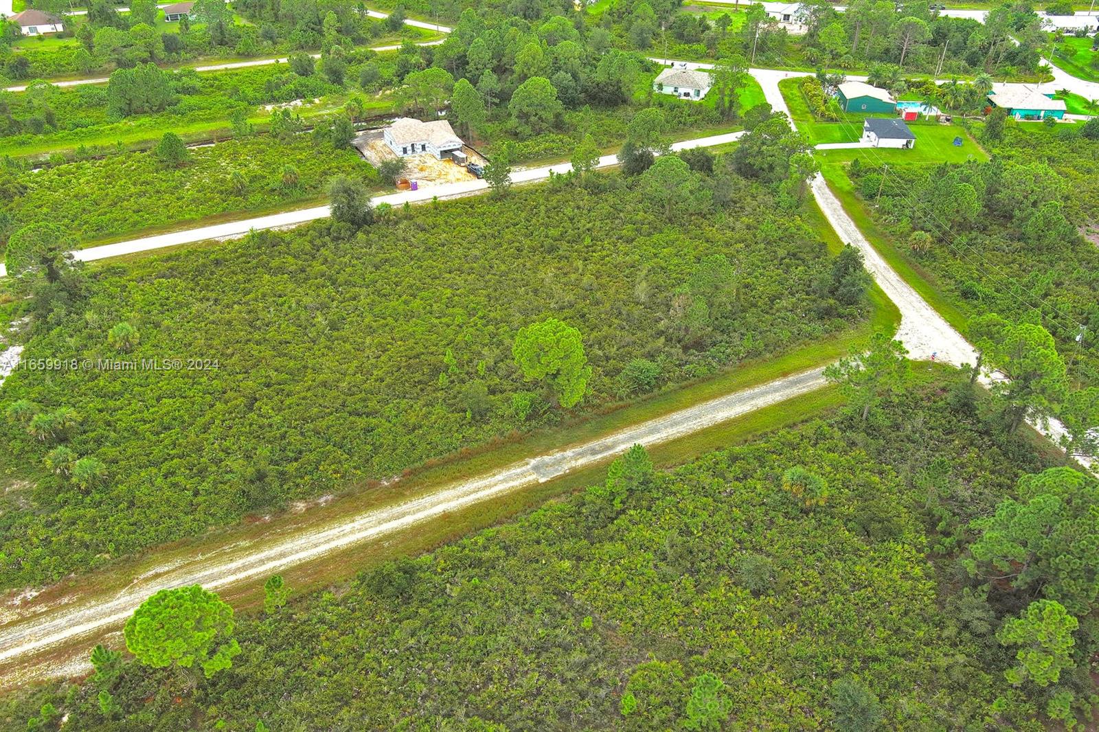 An aerial view shows a large, undeveloped wooded lot with a dirt road running through it — 642 Vasser Ave S, Lehigh Acres FL 33974, LEHIGH ACRES, FL