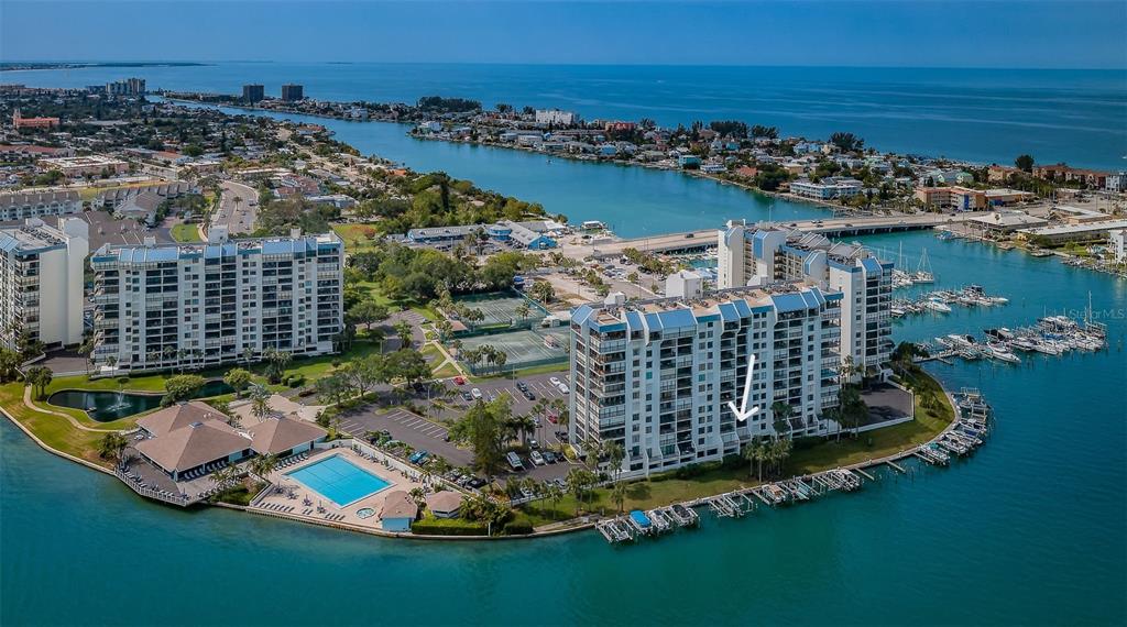 An aerial view shows a waterfront condominium complex with a pool, tennis courts, and boat slips — 9495 BLIND PASS ROAD UNIT 205, ST PETE BEACH, FL