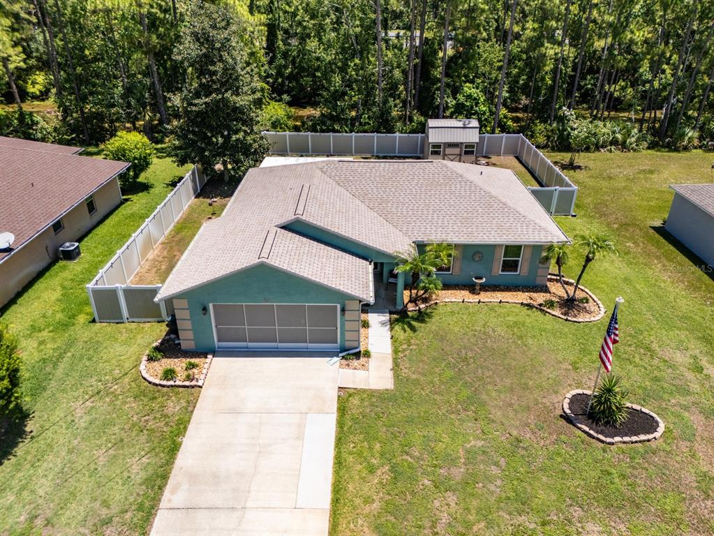 An aerial view shows a teal single-story house with a garage, driveway, and fenced backyard — 69 PICKERING DRIVE, PALM COAST, FL