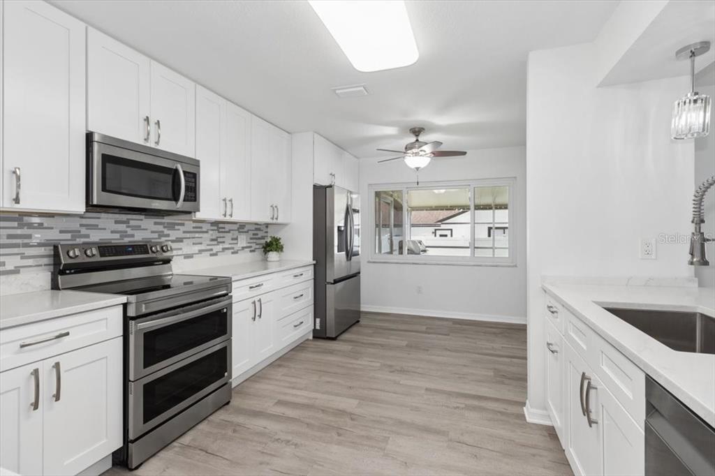 A modern kitchen features white cabinets, stainless steel appliances, and light wood-look flooring — 4102 W BANK AVENUE, TAMPA, FL