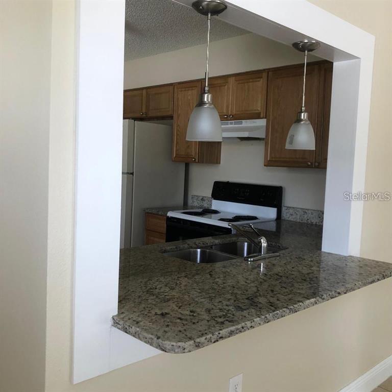 A kitchen with granite countertops, wooden cabinets, and two pendant lights over a breakfast bar — 2839 8 IRON DRIVE UNIT 2839, LAKELAND, FL