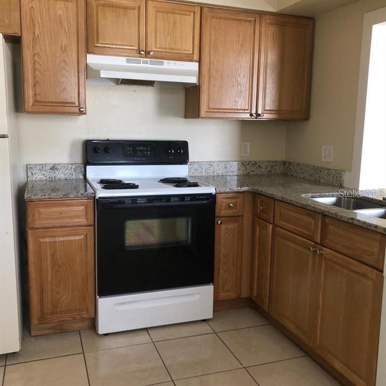 A kitchen features oak cabinets, a black electric stove, and granite countertops — 2839 8 IRON DRIVE UNIT 2839, LAKELAND, FL