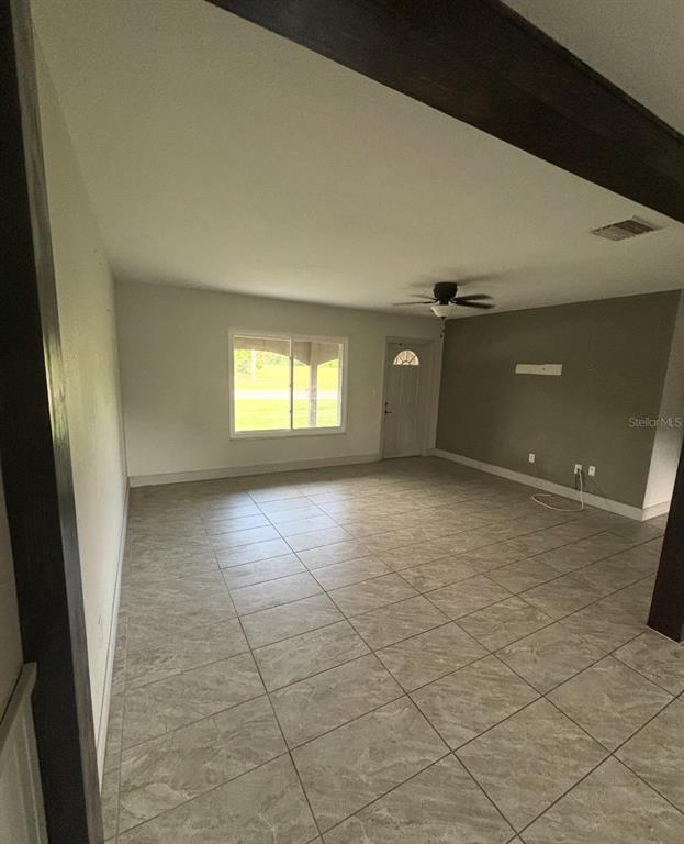 An empty room features light-colored tile flooring, white walls, a dark accent wall, and ceiling beams — 6735 APPOMATTOX DRIVE, NORTH PORT, FL