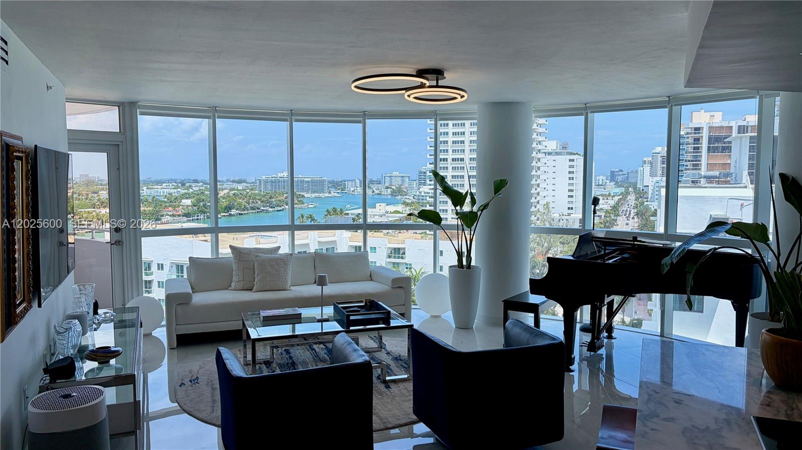 A living room with a grand piano, white sofa, and floor-to-ceiling windows overlooking water — 6301 Collins Ave # 1207, Miami Beach FL 33141, MIAMI BEACH, FL