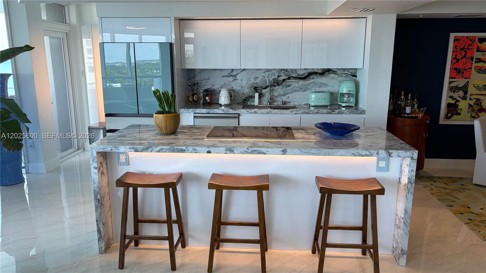 A modern kitchen features a marble waterfall island with three wooden bar stools — 6301 Collins Ave # 1207, Miami Beach FL 33141, MIAMI BEACH, FL