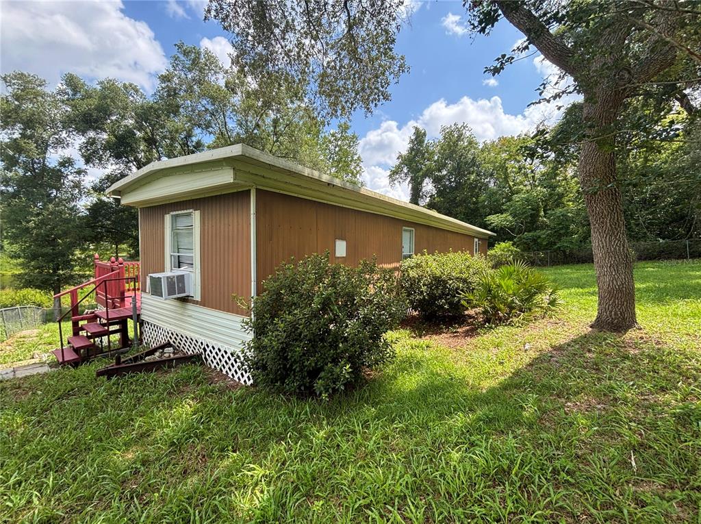 A mobile home with brown siding, a white base, and a red deck sits outdoors — 18225 SE 22ND PLACE, SILVER SPRINGS, FL