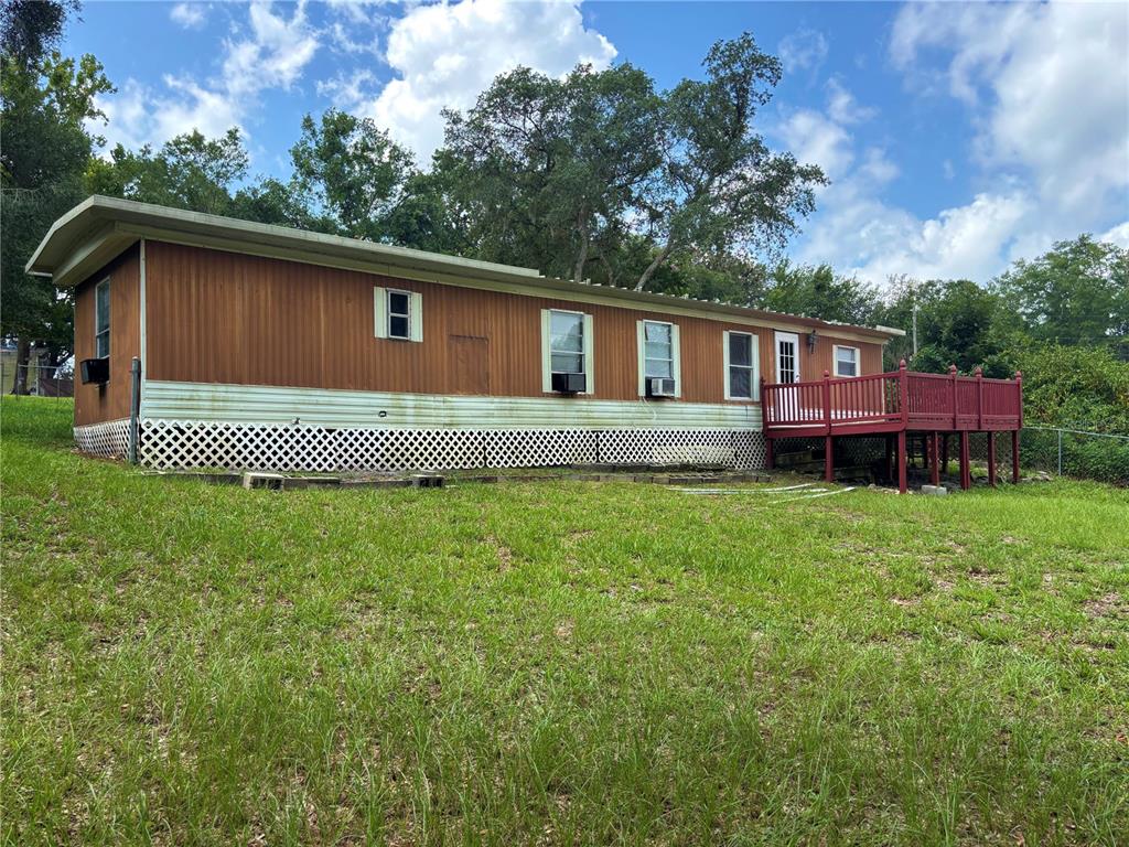 A single-story mobile home with wood-paneled siding and a red wooden deck — 18225 SE 22ND PLACE, SILVER SPRINGS, FL