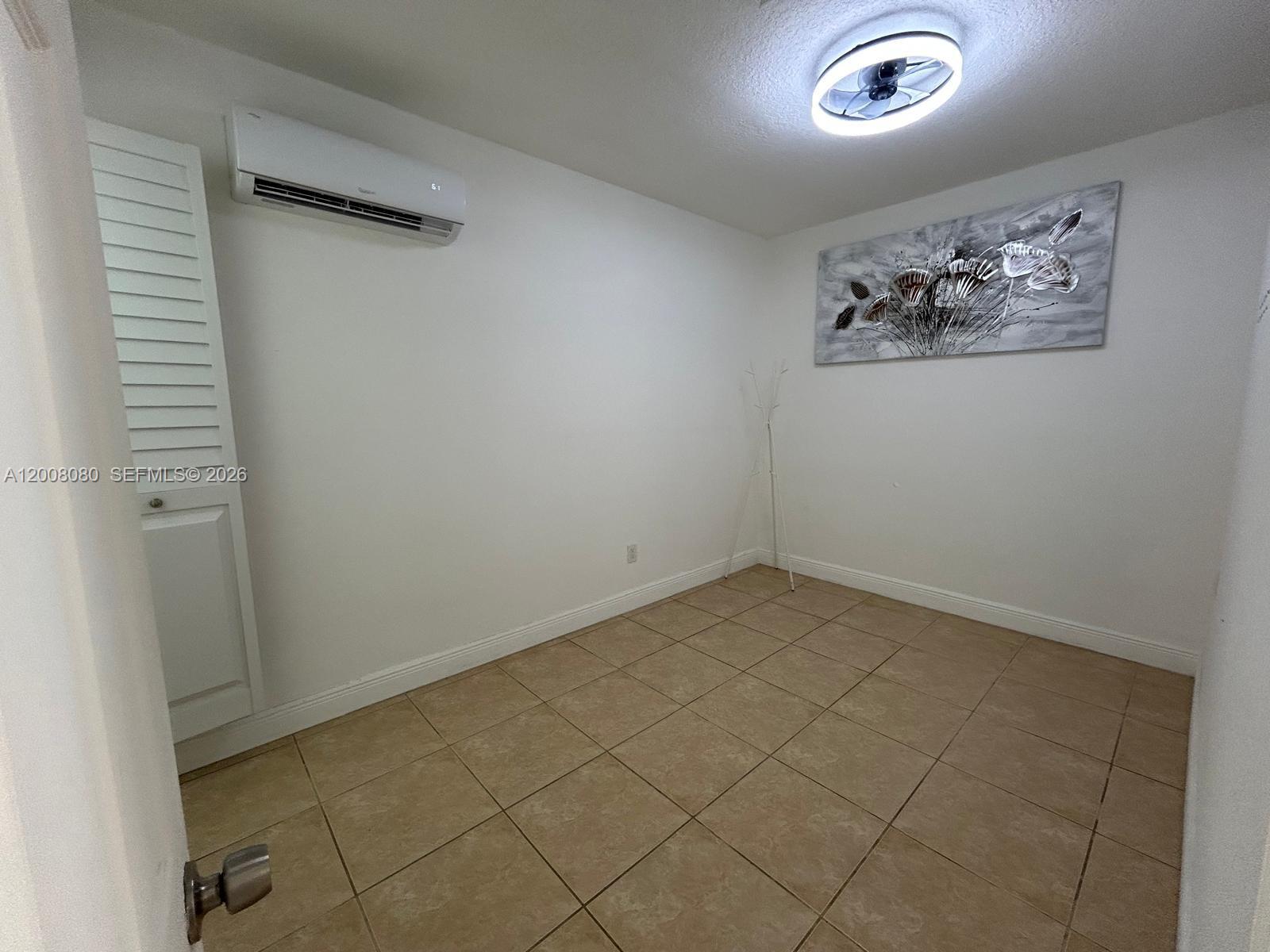 A small room features tan tile flooring, a white wall-mounted air conditioner, and ceiling lighting — 14731 SW 170th Ter # 1, Miami FL 33187, MIAMI, FL