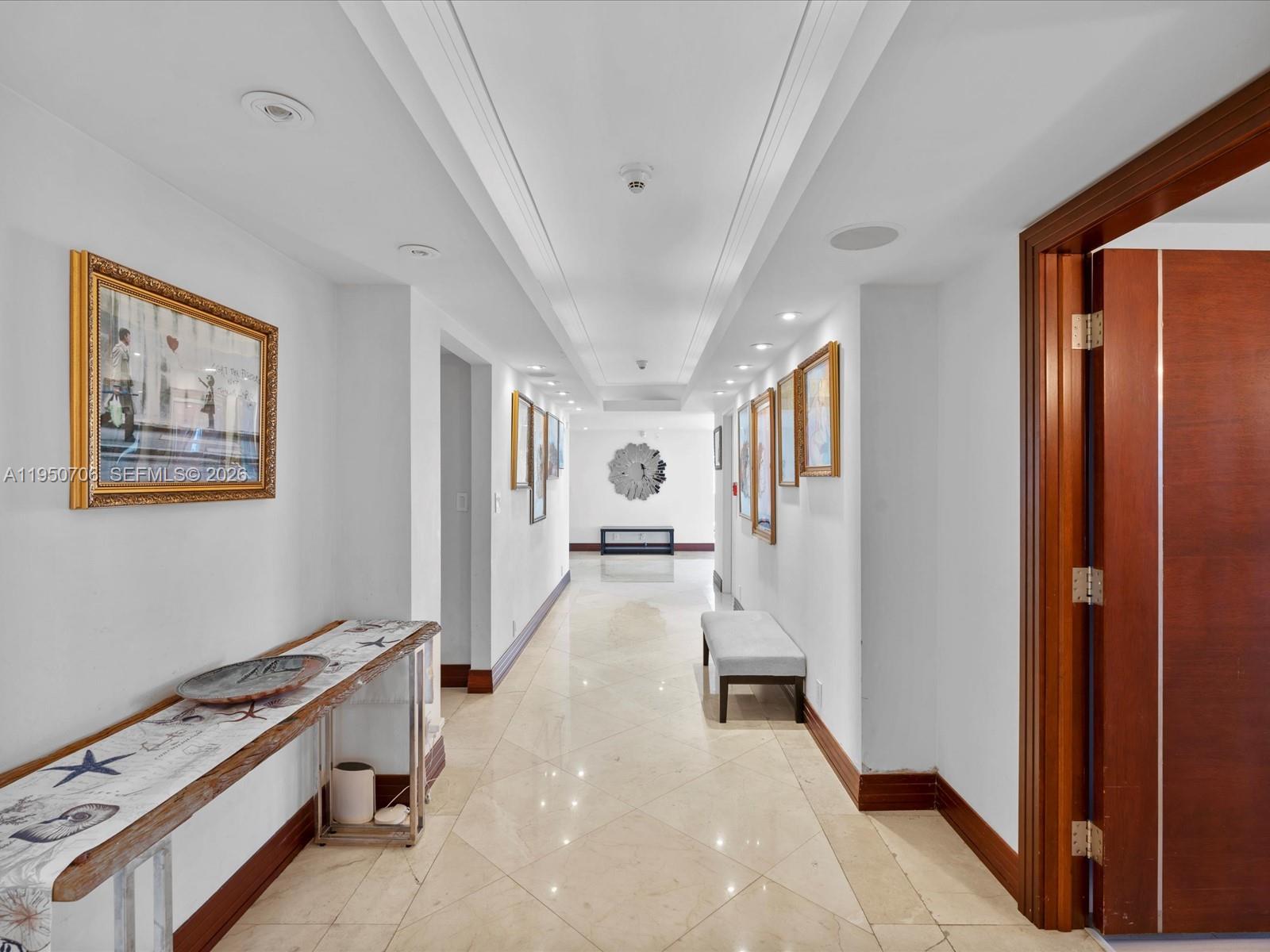 A long, tiled hallway features a console table, a bench, and framed artwork on walls — 5660 Collins Ave # 18A, Miami Beach FL 33140, MIAMI BEACH, FL