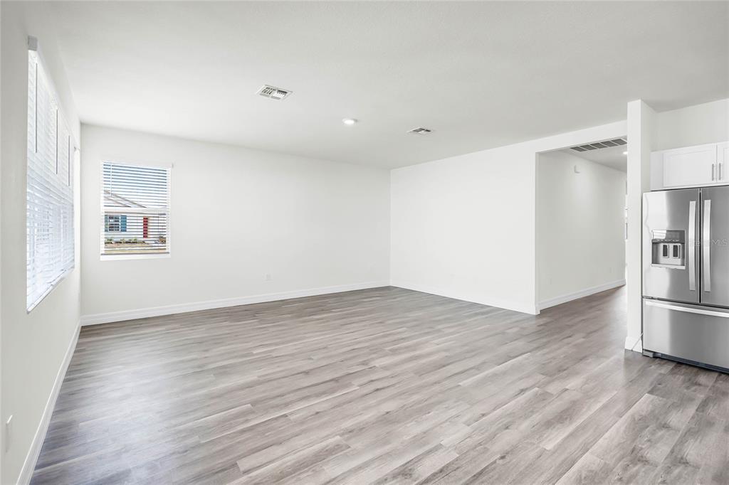 An open-concept living area features light gray wood-look flooring and a stainless steel refrigerator — 5231 LIGONBERRY STREET, LAKELAND, FL