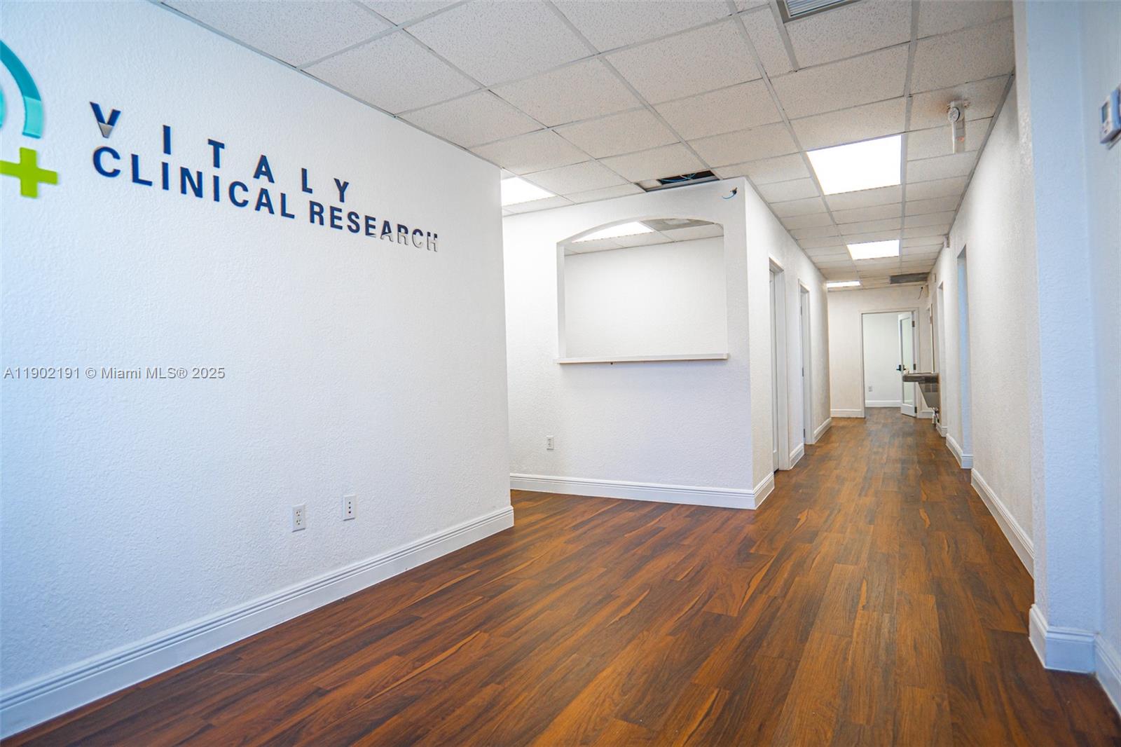 A clinical office hallway features wood-look flooring, white walls, and a reception cutout — 3401 NW 7th St, Miami FL 33125, MIAMI, FL