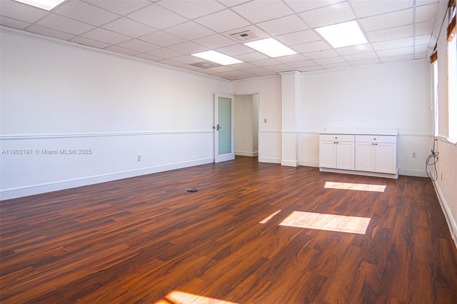 An empty office room features wood-look flooring, white walls, a drop ceiling, and built-in cabinets — 3401 NW 7th St, Miami FL 33125, MIAMI, FL