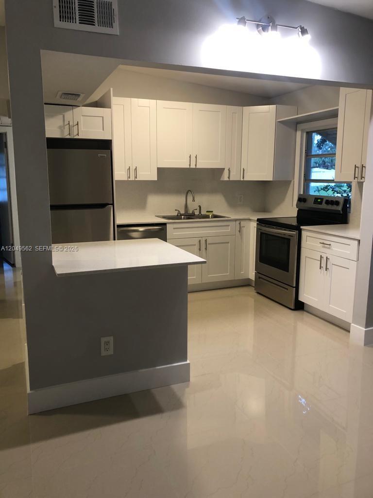 A kitchen features white shaker cabinets, stainless steel appliances, and a white peninsula countertop — 2106 79th CT # A, Vero Beach FL 32966, VERO BEACH, FL