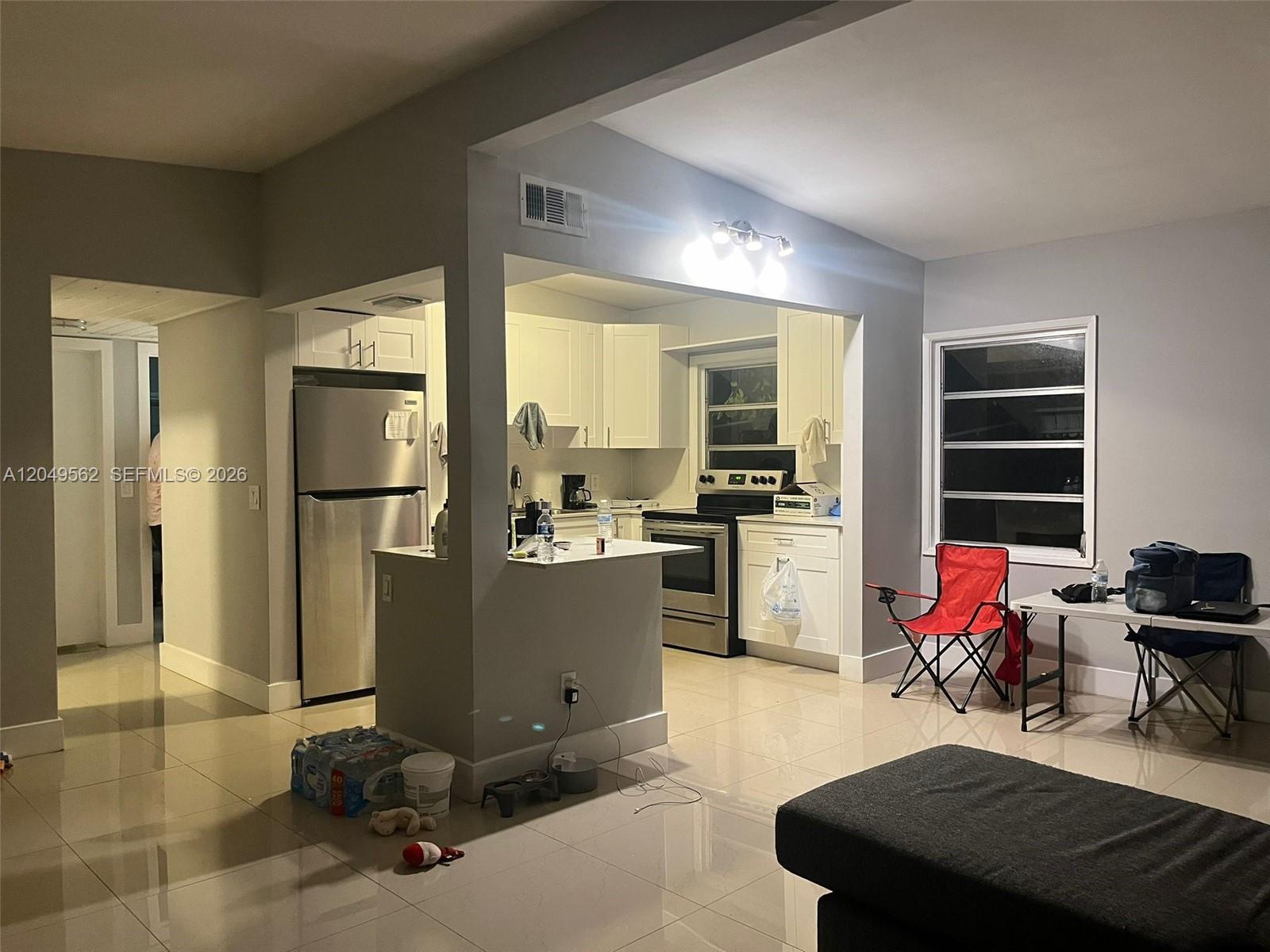 A kitchen with white cabinets and stainless steel appliances opens into a tiled living area — 2106 79th CT # A, Vero Beach FL 32966, VERO BEACH, FL
