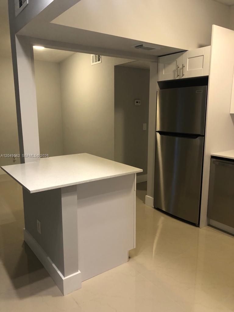 A kitchen features a white island, stainless steel refrigerator, and light-colored tile flooring — 2106 79th CT # A, Vero Beach FL 32966, VERO BEACH, FL