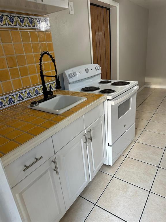 A kitchen features white cabinets, a yellow tiled countertop, a sink, and a white stove — 3407 N AVENIDA REPUBLICA DE CUBA UNIT A, TAMPA, FL