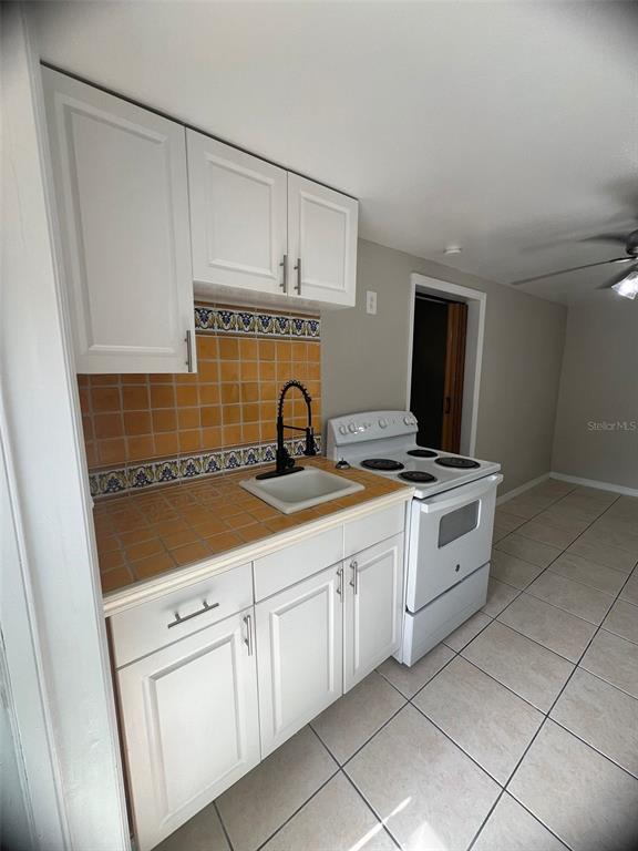 A kitchen features white cabinets, a yellow tiled backsplash, a sink, and a white stove — 3407 N AVENIDA REPUBLICA DE CUBA UNIT A, TAMPA, FL