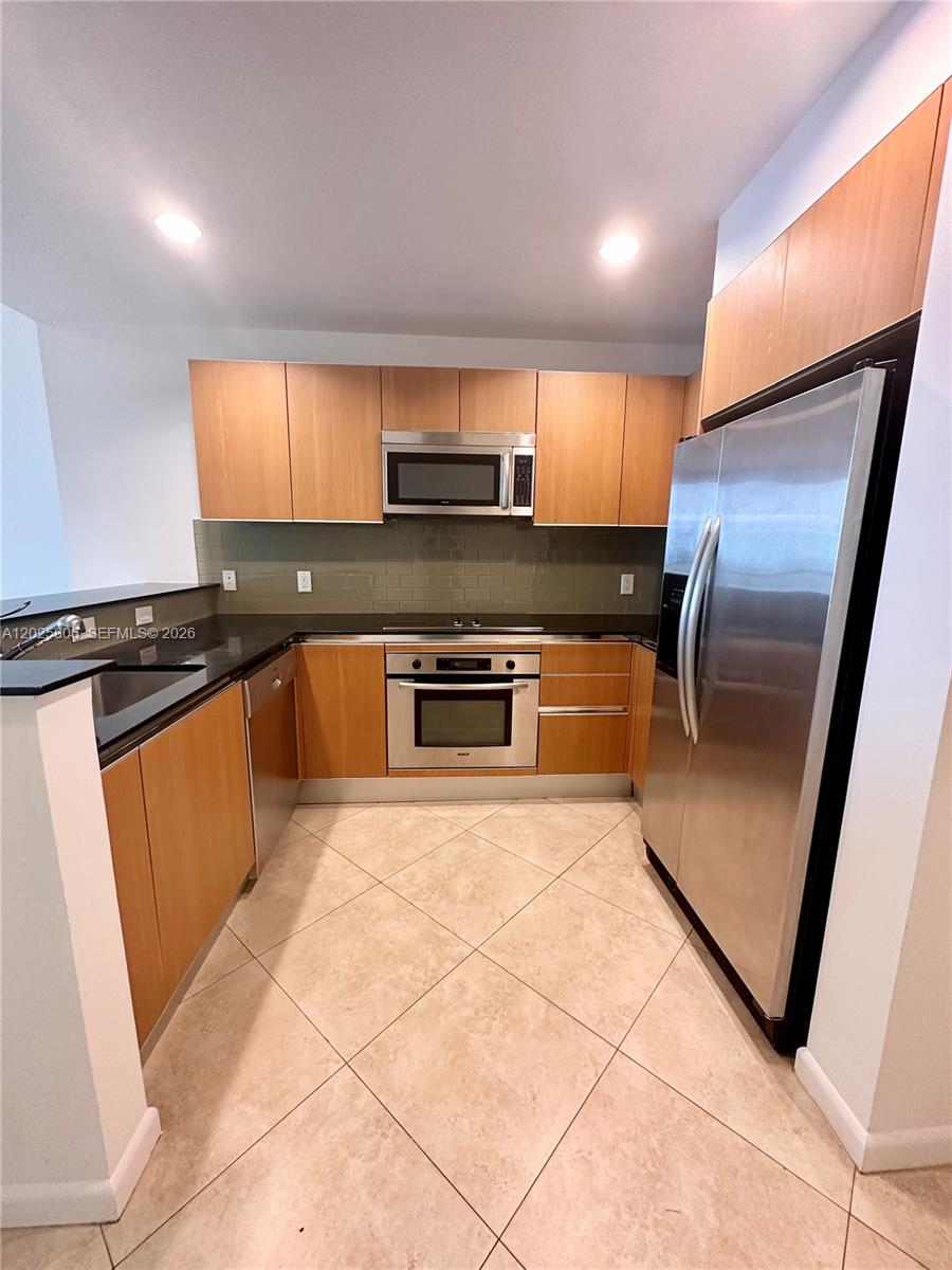 A kitchen features light wood cabinets, stainless steel appliances, and a dark stone countertop — 1060 Brickell Ave # 2515, Miami FL 33131, MIAMI, FL