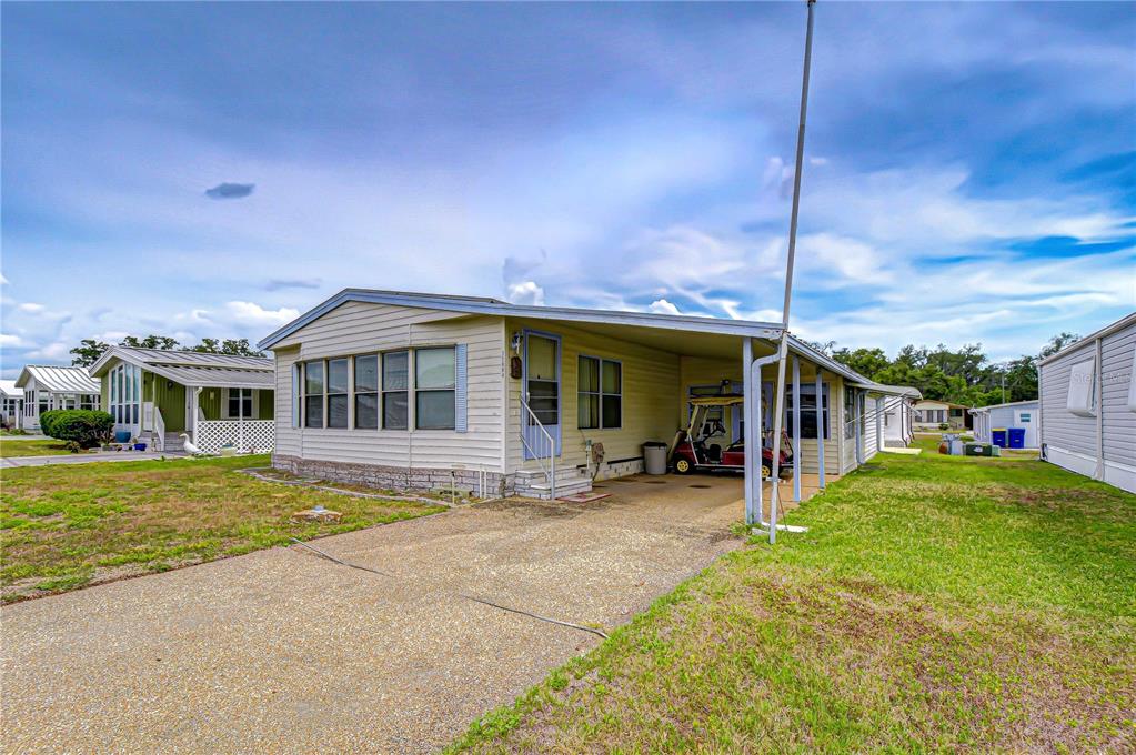 A single-story manufactured home with a carport and a concrete driveway under a blue sky — 35804 BRISA DRIVE, ZEPHYRHILLS, FL
