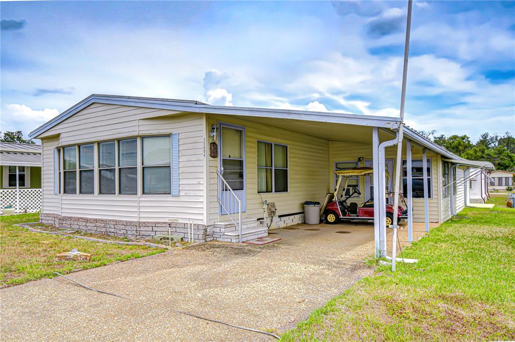 A single-story mobile home with light siding, a carport, and a golf cart parked underneath — 35804 BRISA DRIVE, ZEPHYRHILLS, FL
