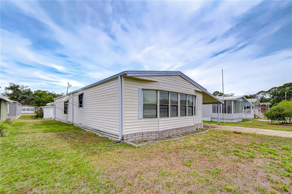 A side view of a single-story manufactured home with light-colored siding and a brick-patterned base — 35804 BRISA DRIVE, ZEPHYRHILLS, FL