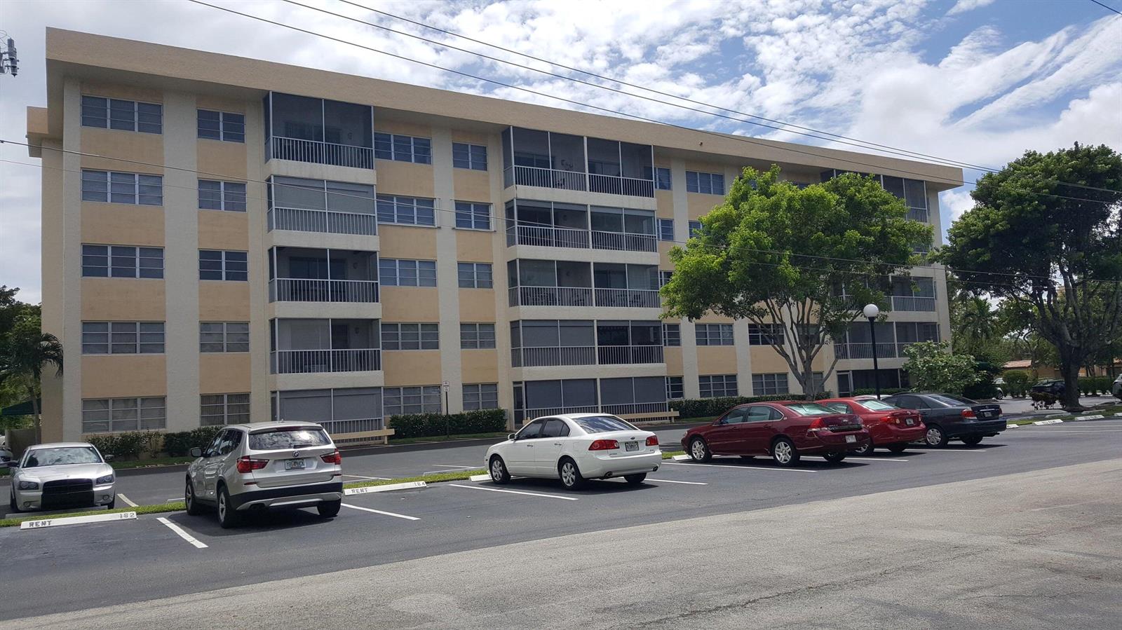 A multi-story apartment building with screened balconies sits behind a parking lot with several cars — 50 SW 3rd Avenue # 5080, Boca Raton FL 33432, BOCA RATON, FL