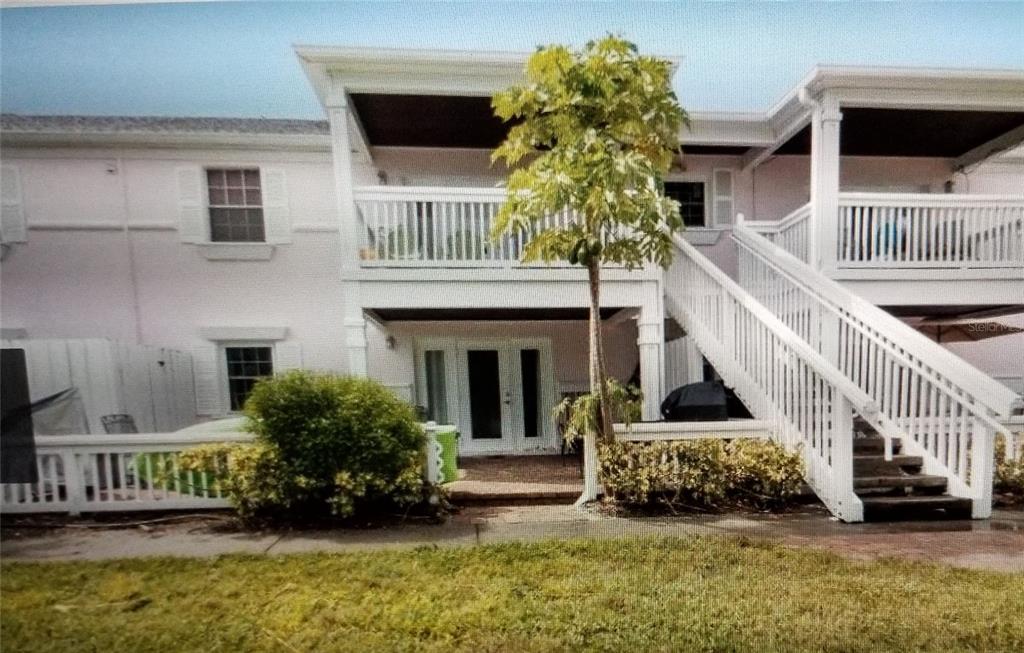 A two-story townhouse exterior features a white balcony, an outdoor staircase, and a ground-level patio — 213 SEAHORSE DRIVE SE UNIT D, ST PETERSBURG, FL