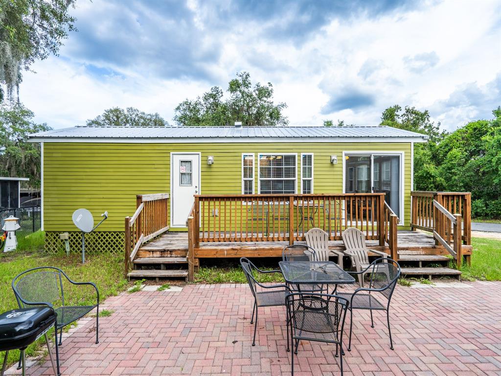 A lime green mobile home features a wooden deck and a brick patio with outdoor furniture — 15991 NE 243RD PLACE ROAD UNIT 32, FORT MC COY, FL