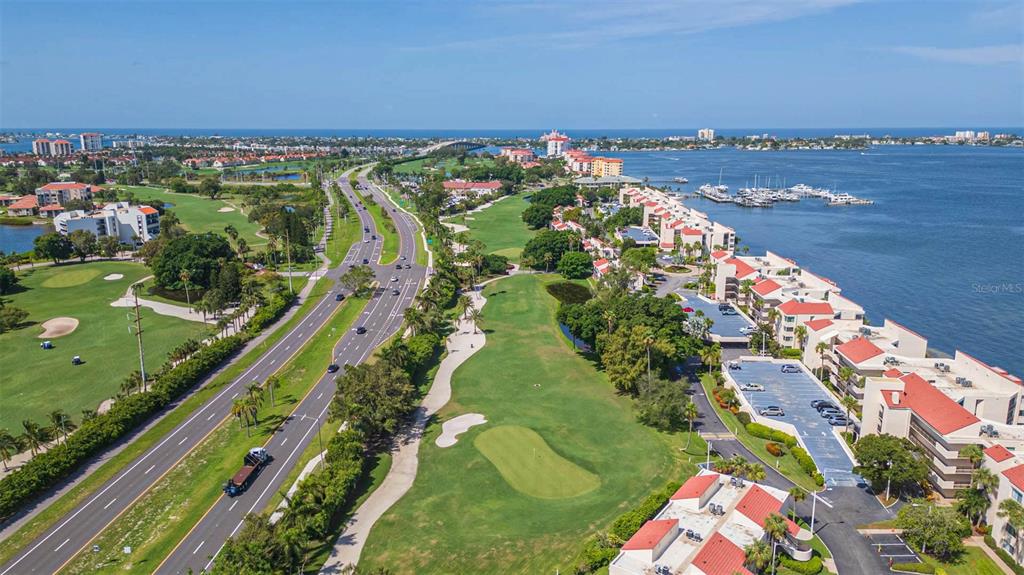 An aerial view shows a multi-lane road running alongside a golf course and waterfront condominiums — 5510 PUERTA DEL SOL BOULEVARD S UNIT 132, ST PETERSBURG, FL