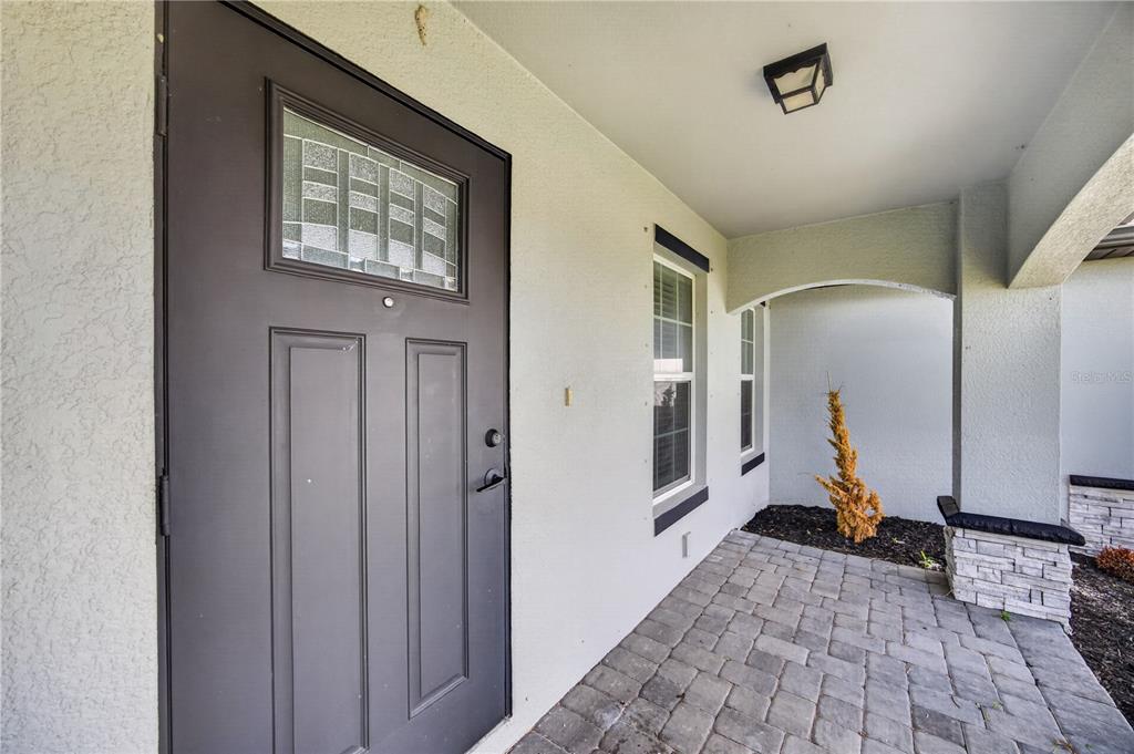 A gray front door with a glass insert opens onto a paved porch with stucco walls — 4238 NW 34TH LANE, CAPE CORAL, FL